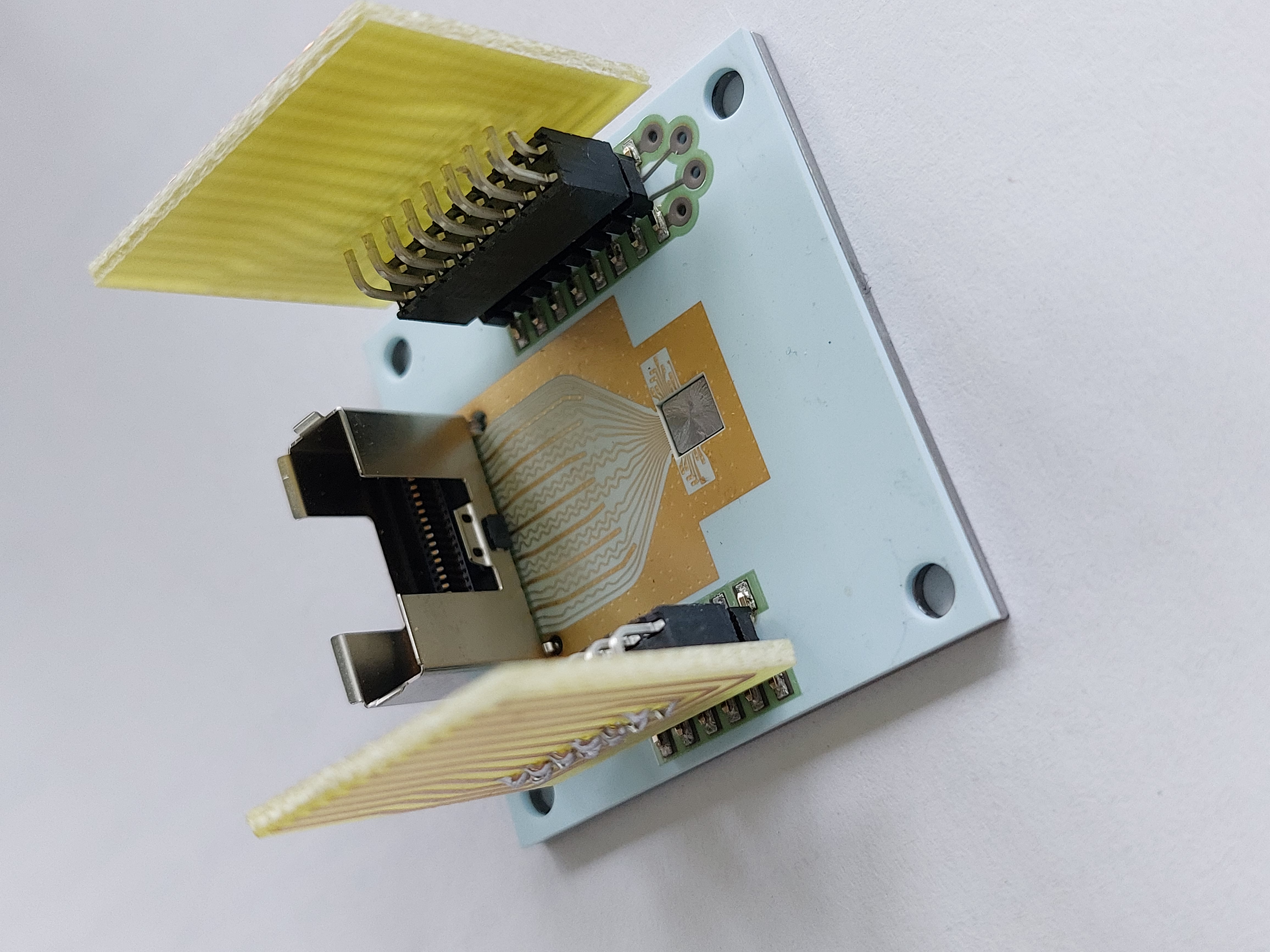 A ceramic printed circuit board (PCB) is bonded to a molybdenum heatsink. The PCB carries the VCSEL and driver chip (center). The wings are plugs for thermal management components.